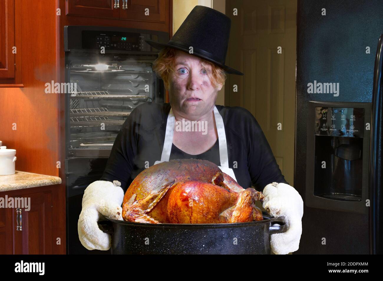 Donna in piedi in cucina indossando pellegrino hat e grembiule con bruciature viso e capelli tenendo una teglia. Foto Stock