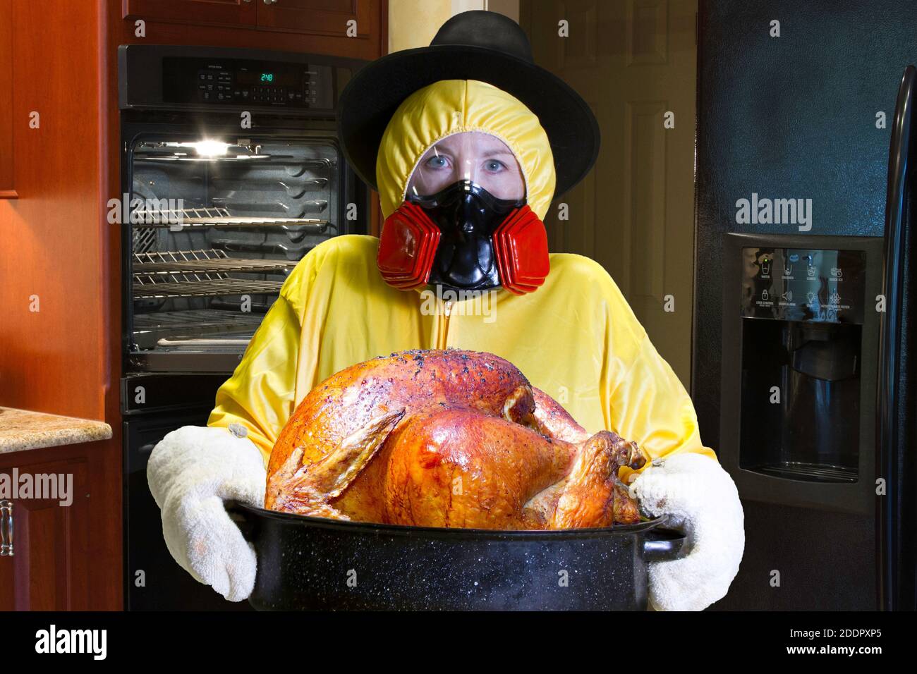 La donna in giallo HazMat suit e indossare il respiratore pellegrino hat in piedi accanto ad aprire il forno in cucina. Foto Stock