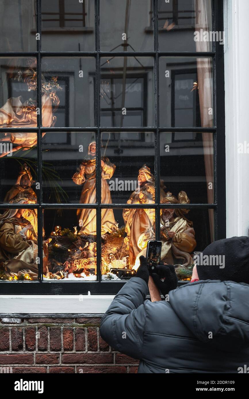 Deventer, Paesi Bassi, 15 dicembre 2018:Woman usa il suo telefono per scattare una foto di una scena di Natale illuminata dietro una finestra di una casa a Deventer Foto Stock