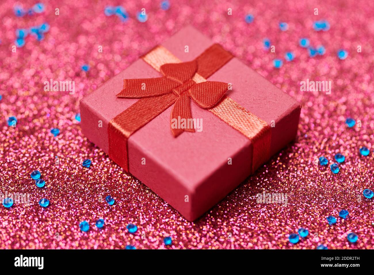 Confezione regalo rossa con glitter natalizio. Piccola scatola chiusa con prua e regalo per anniversario o matrimonio. Confezione regalo a sorpresa per la persona amata. Foto Stock