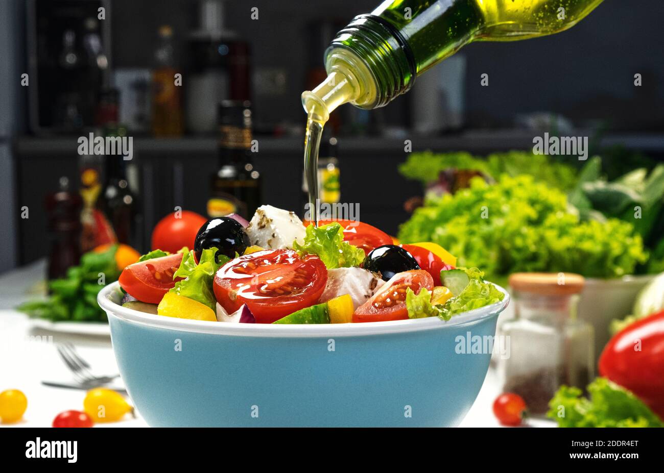 Versare l'olio d'oliva su insalata di verdure fresche, insalata greca su tavola bianca Foto Stock