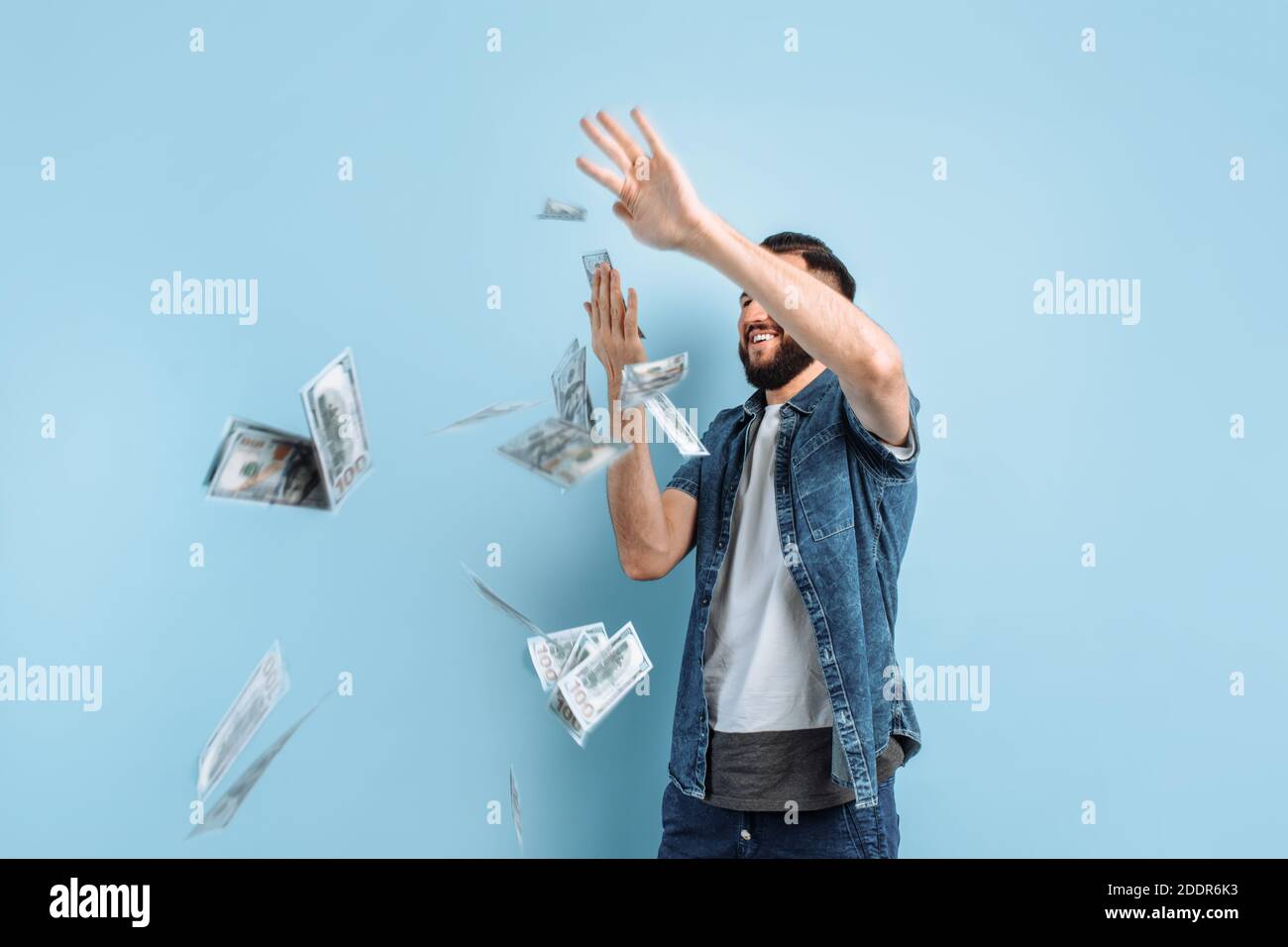 Ritratto di un felice giovane uomo bearded che gettava le banconote isolato su sfondo blu Foto Stock