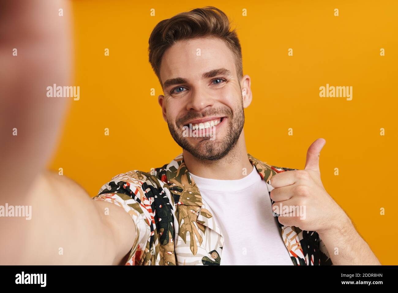 Allegro bel ragazzo gesturing pollice in su mentre scattano foto selfie isolato su sfondo giallo Foto Stock