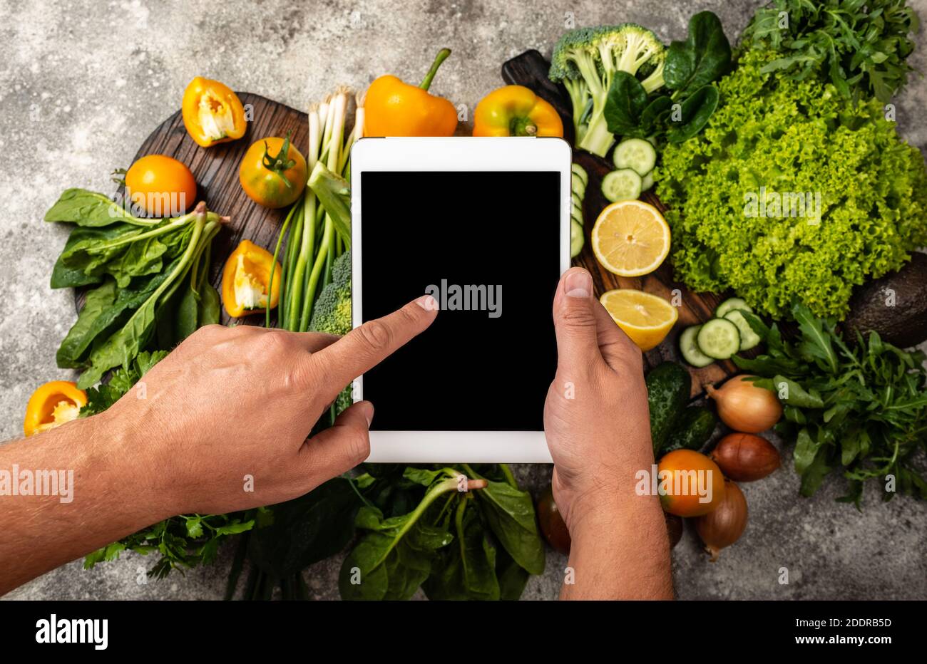 Ordine consegna cibo on-line concetto. Le mani maschili tengono il computer tablet con uno schermo vuoto sulle verdure fresche. Primo piano Foto Stock