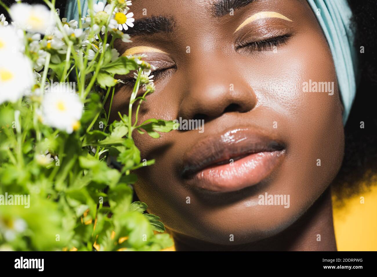 primo piano di giovane donna afro-americana con bouquet camomilla isolato giallo acceso Foto Stock