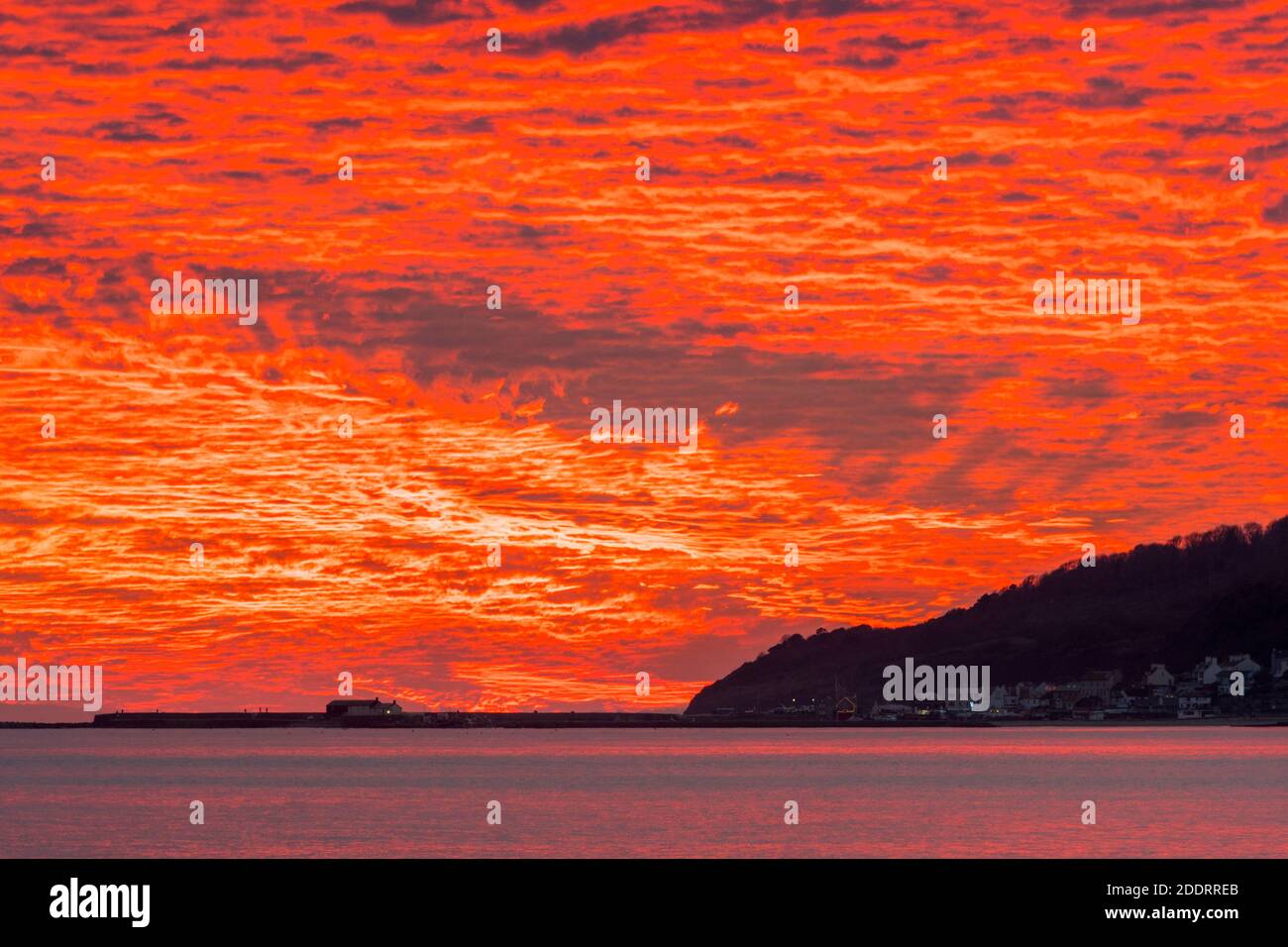 Charmouth, Dorset, Regno Unito. 26 novembre 2020. Uno spettacolare tramonto rosso fuoco sul porto di Cobb e Lyme Regis in Dorset vista dalla spiaggia di Charmouth alla fine di una giornata di sole Picture Credit: Graham Hunt/Alamy Live News Foto Stock