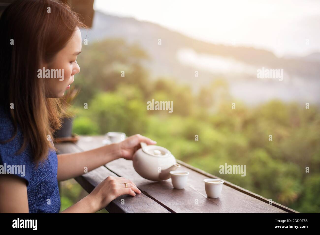 donna asiatica che versa una tazza di tè su un tavolo di legno di fronte alla splendida piantagione di tè e montagna al mattino ora Foto Stock