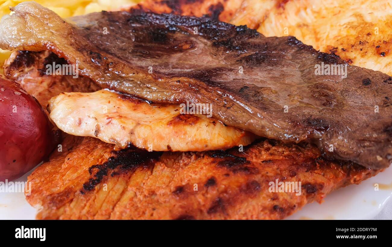 Primo piano di bistecche grigliate miste su un piatto, con carne di maiale, manzo, pollo e patate, focalizzazione selettiva Foto Stock