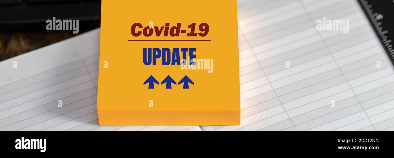 COVID-19 AGGIORNAMENTO testo su adesivo giallo su sfondo desktop, formato banner. Concetto di coronavirus Foto Stock