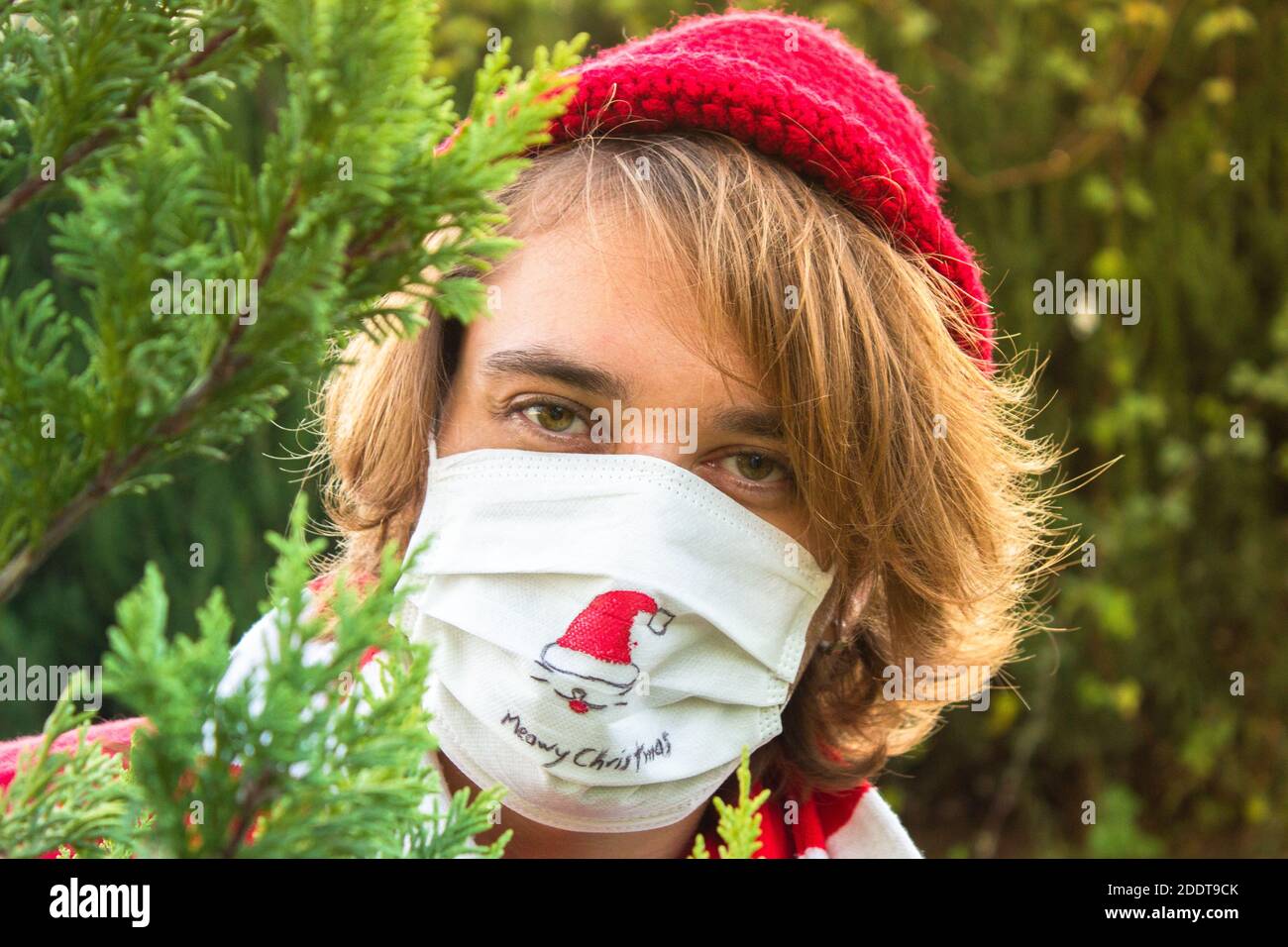 Giovane uomo che festeggia il Natale con maschera medica protettiva per la pandemia di covid-19. Il giovane disegna il cappello di santa su una maschera facciale e celebra C. Foto Stock