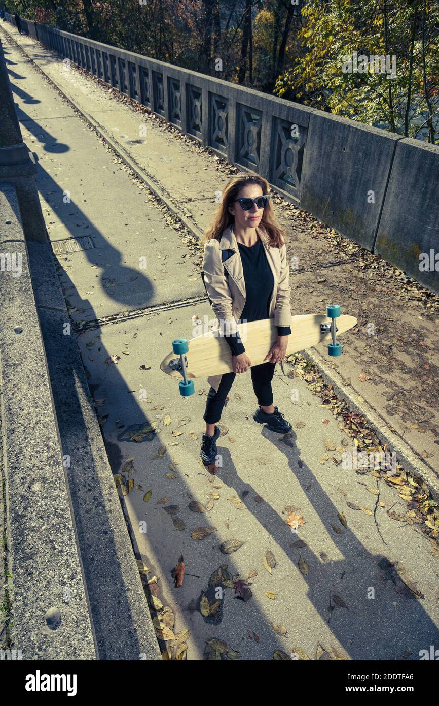Donna attiva che tiene il longboard. Concetto di stile di vita urbano. Foto Stock