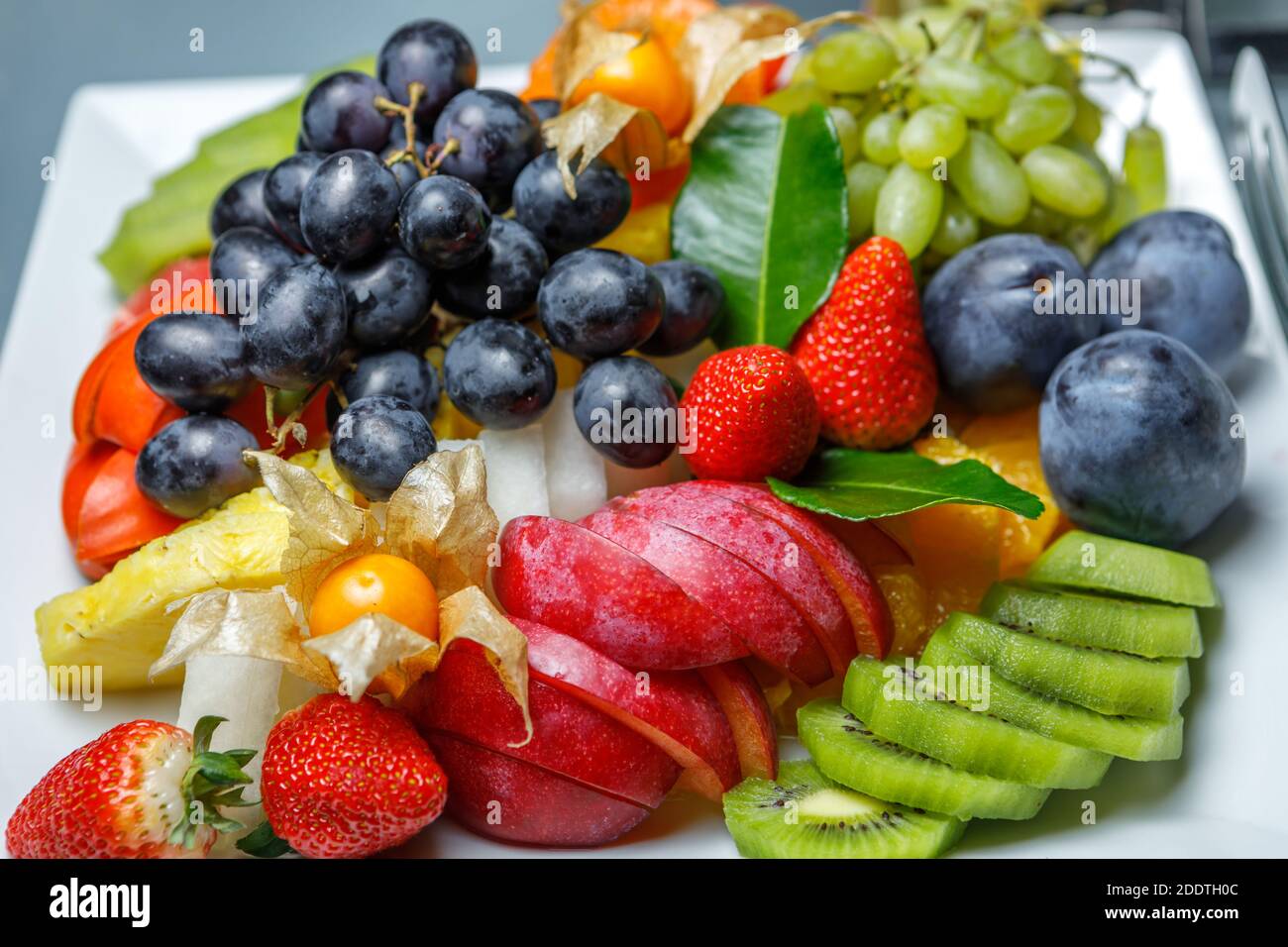 Frutta a fette assortite, uva bianca e nera, kiwi, prugne, ananas, fragole e fisalis sono su un piatto. La vista dall'alto. Foto Stock