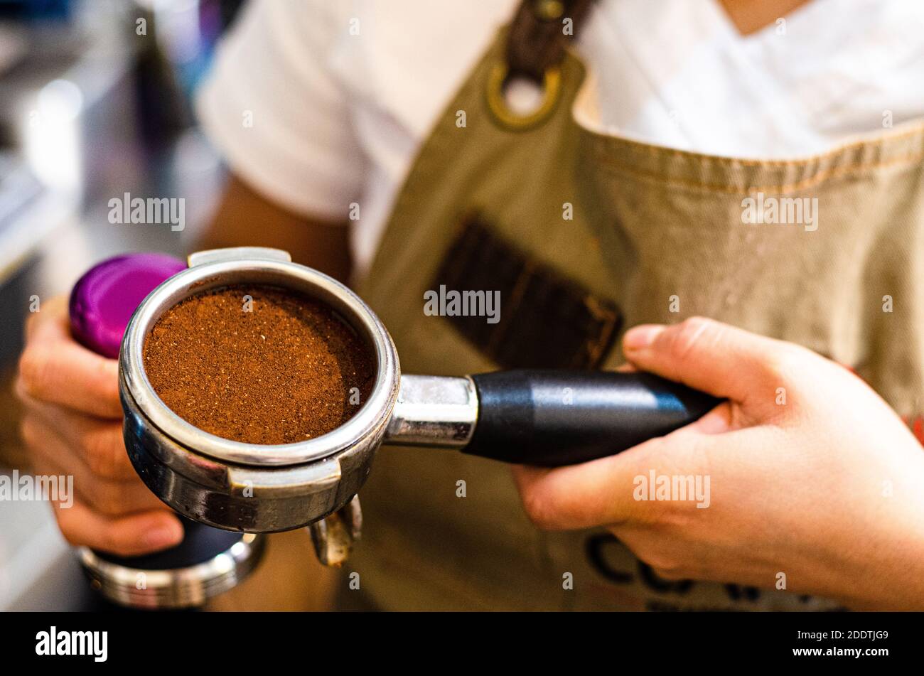 Primo piano del barista femminile che tiene il caffè macinato a mano per la preparazione di espresso, servizio e concetto di preparazione. Foto Stock