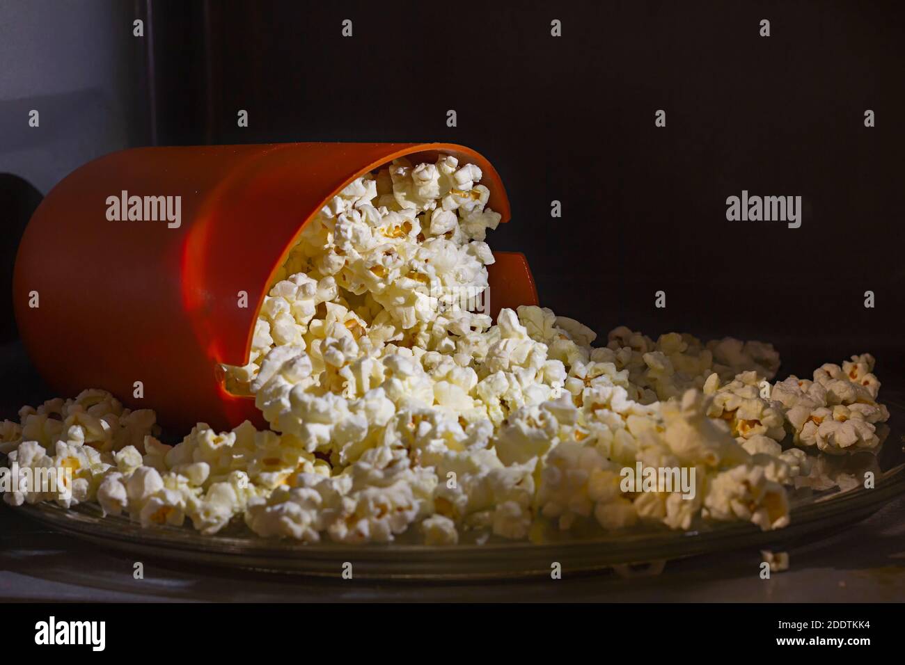 Secchio di silicone arancione riempito con popcorn cucinato in casa all'interno di un forno a microonde. Secchiello in silicone speciale per la cottura a microonde dei popcorn a casa. Foto Stock