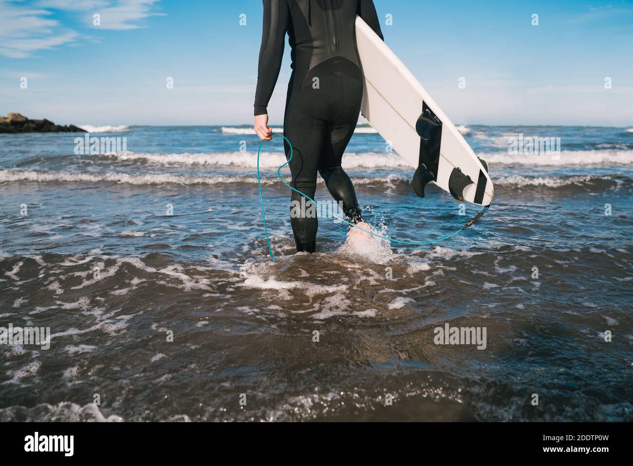 Surfista che entra in acqua con la sua tavola da surf. Foto Stock