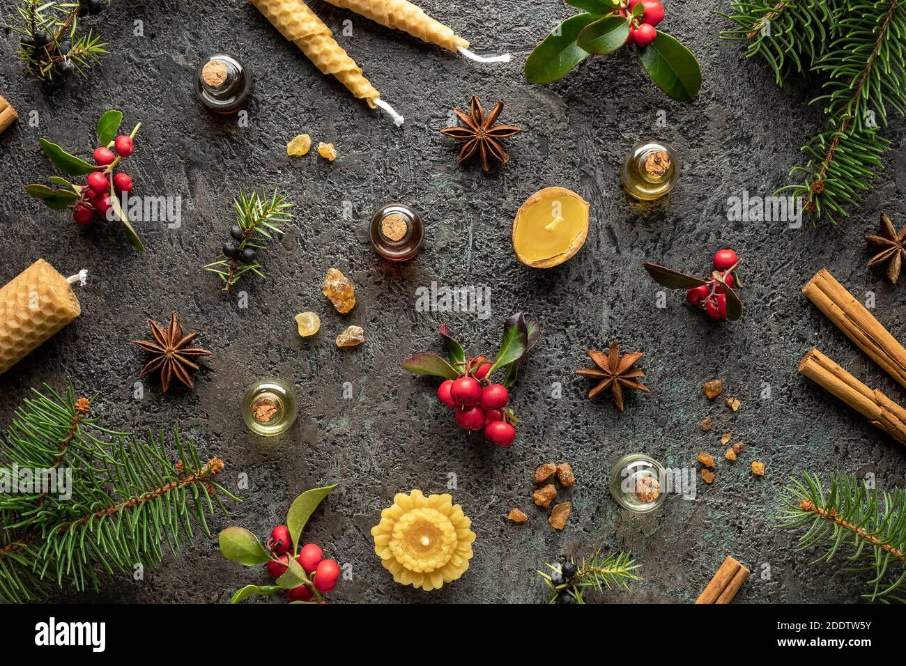 Sfondo natalizio con bottiglie di olio essenziale con incenso, verde inverno, ginepro, cannella e abete rosso su sfondo scuro Foto Stock