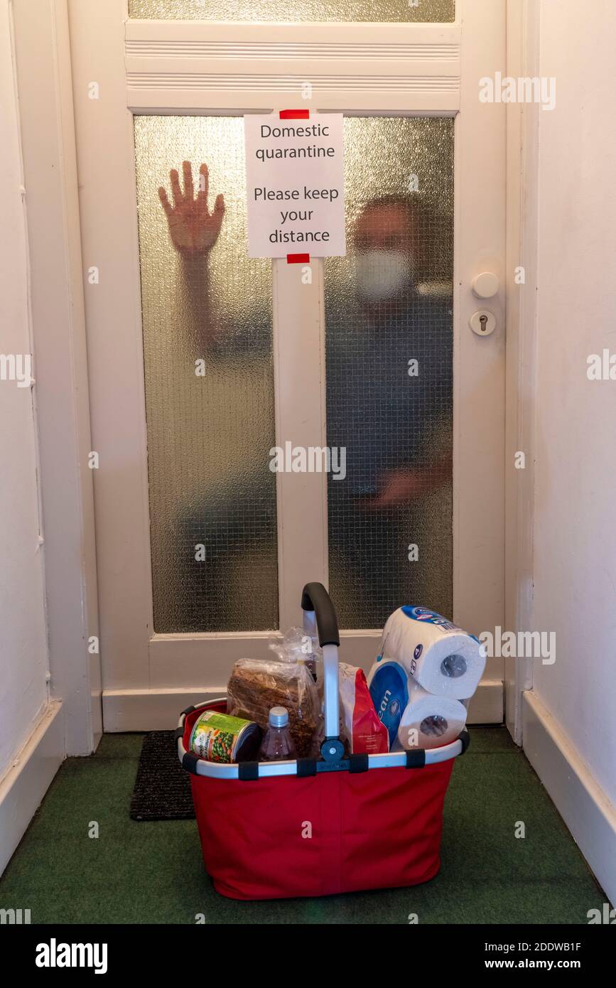 Immagine simbolica quarantena domestica, uomo sospettato di infezione corona, a casa in isolamento, segnale di avvertimento per i visitatori alla porta piatta, comunicato Foto Stock