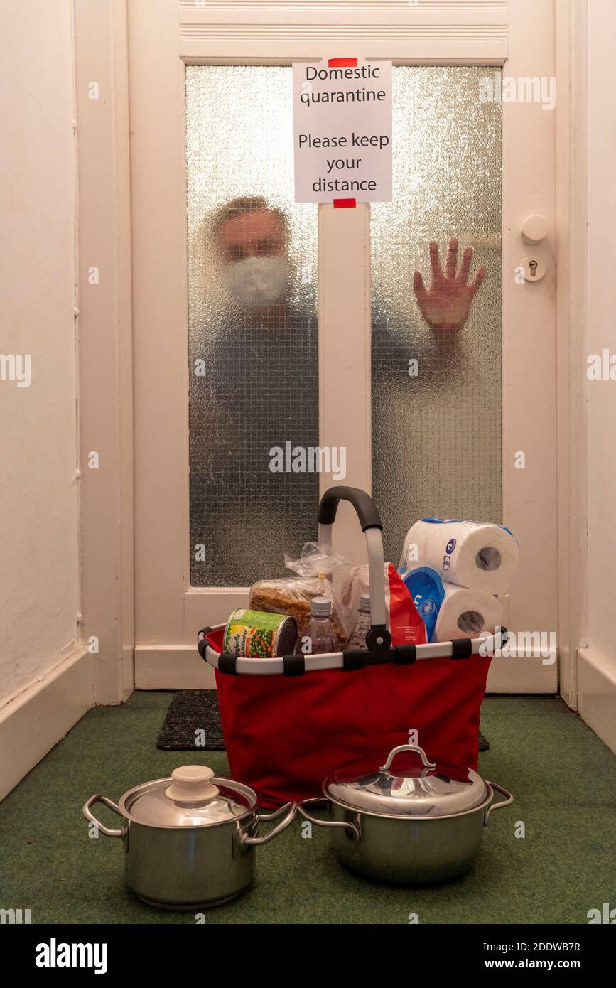 Immagine simbolica quarantena domestica, l'uomo è sospettato di infezione corona, a casa in isolamento, segnale di avvertimento per i visitatori alla porta piatta, comunicat Foto Stock