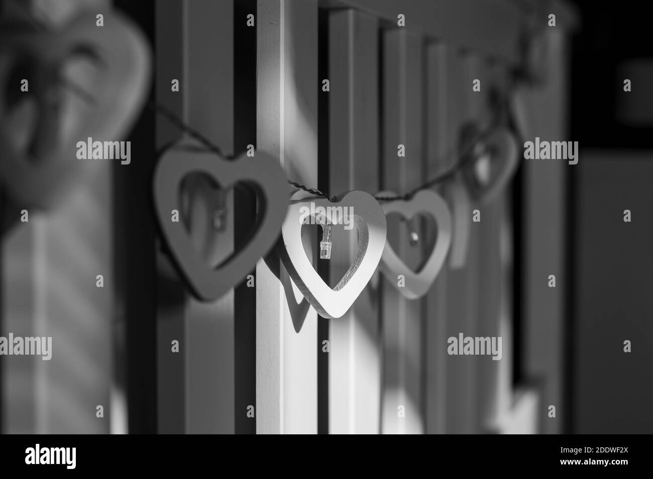 Cuori in legno con le luci appese alla testata. Cuori di legno in fila. Fotografia in bianco e nero. Foto Stock
