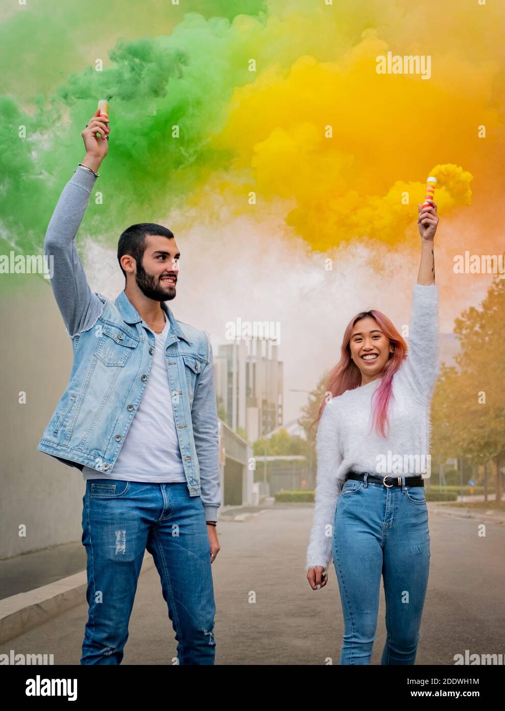 Bei ragazzi si levano in piedi strada e tenere luce su colorato Bombe di fumo - amici felici che si divertono per strada con bombe di fumo multicolore Foto Stock