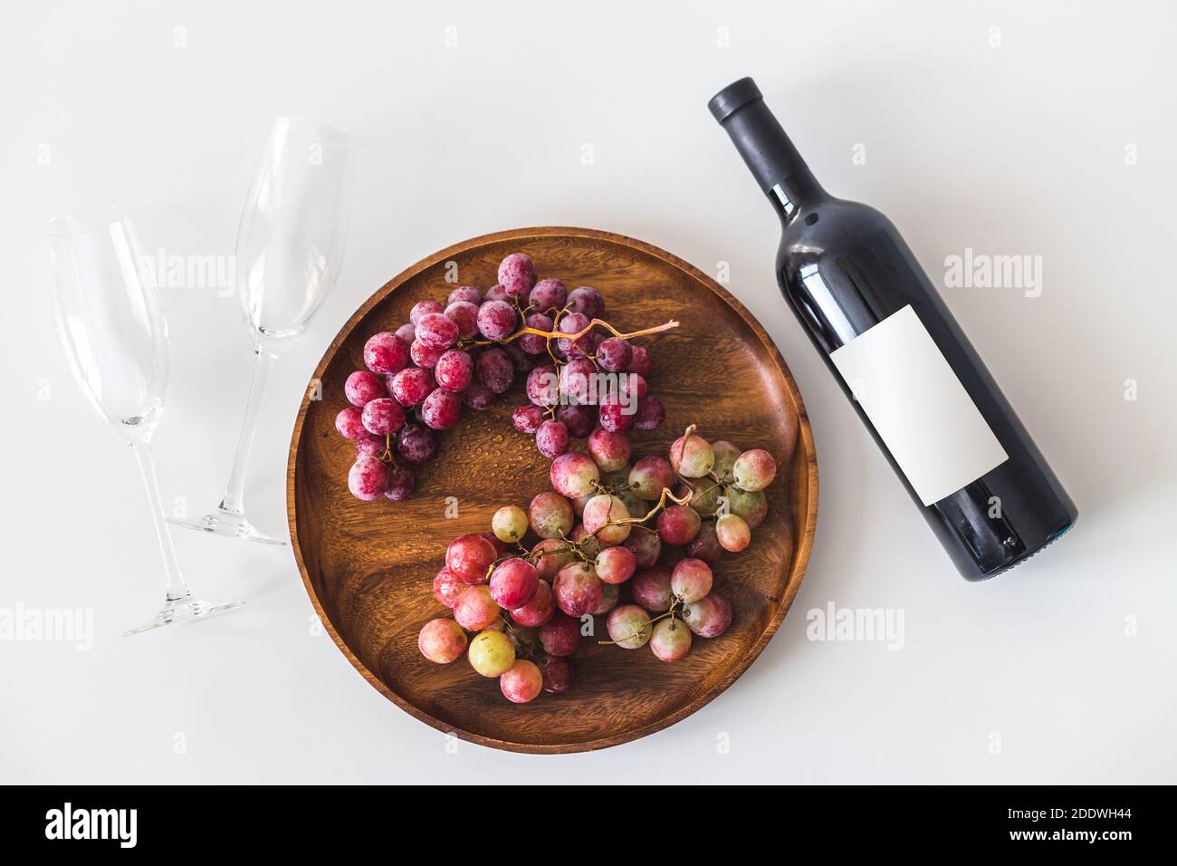 Bottiglia di vino rosso e grandi uve fresche di borgogna su piatto di legno su sfondo bianco, spazio copia piatto, vista dall'alto, mockup Foto Stock