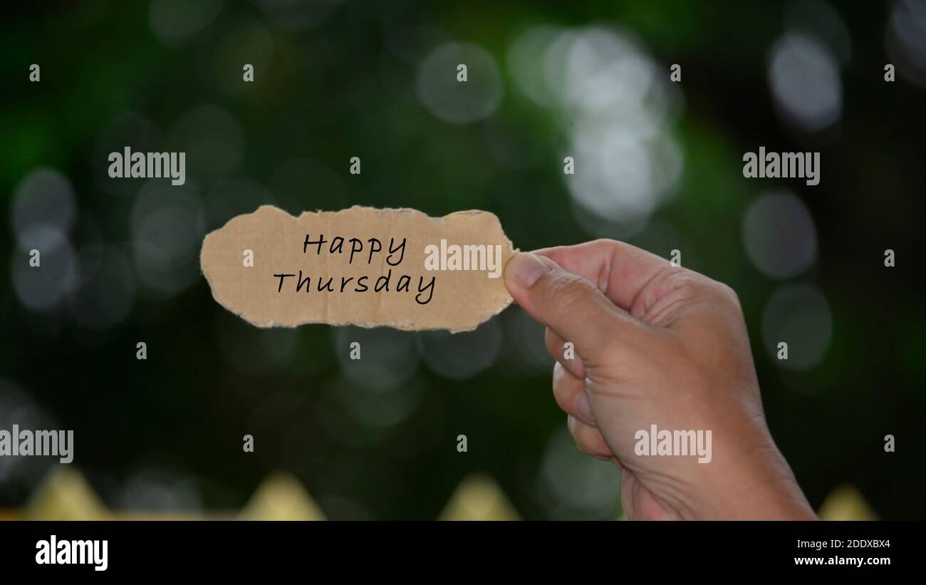 Happy Thursday testo su mani che tiene strappato carta con sfocato sfondo scuro. Giovedì Preventivo Foto Stock