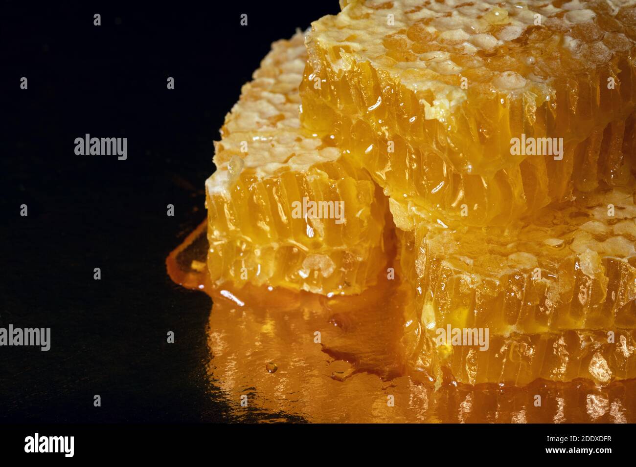Pezzi dorati di nido d'ape fresco con gocce di miele sopra sfondo scuro sfocato Foto Stock