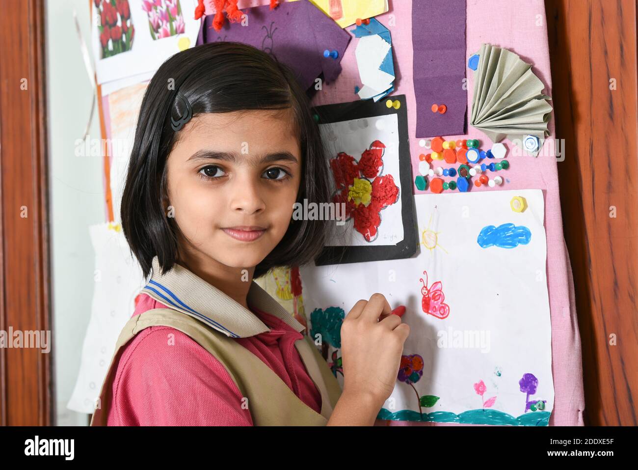 Felice sorridente indiano scuola ragazzina studente imparare disegno decorando bacheca in sala classe d'arte, bambino che indossa la scuola uniforme India. Istruzione Foto Stock