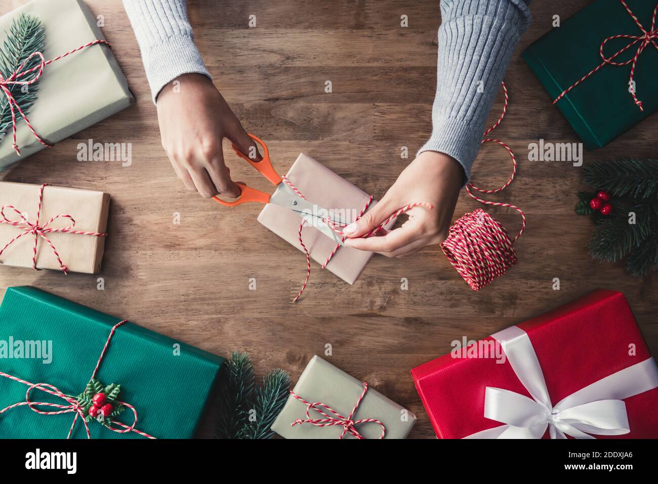 Donna che lega la corda intorno alla scatola del regalo dopo l'imballaggio con carta sul tavolo di legno, che si prepara per celebrare il Natale Foto Stock