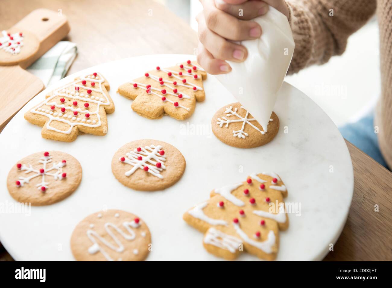 Giovane donna che decora biscotti natalizi fatti in casa con pan di zenzero e glassa reale zucchero su piatto bianco Foto Stock