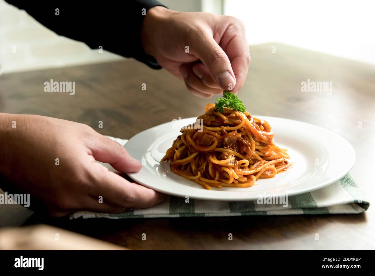 Chef che mette il prezzemolo in cima a deliziosi spaghetti bolognesi in un piatto bianco sul tavolo da cucina Foto Stock