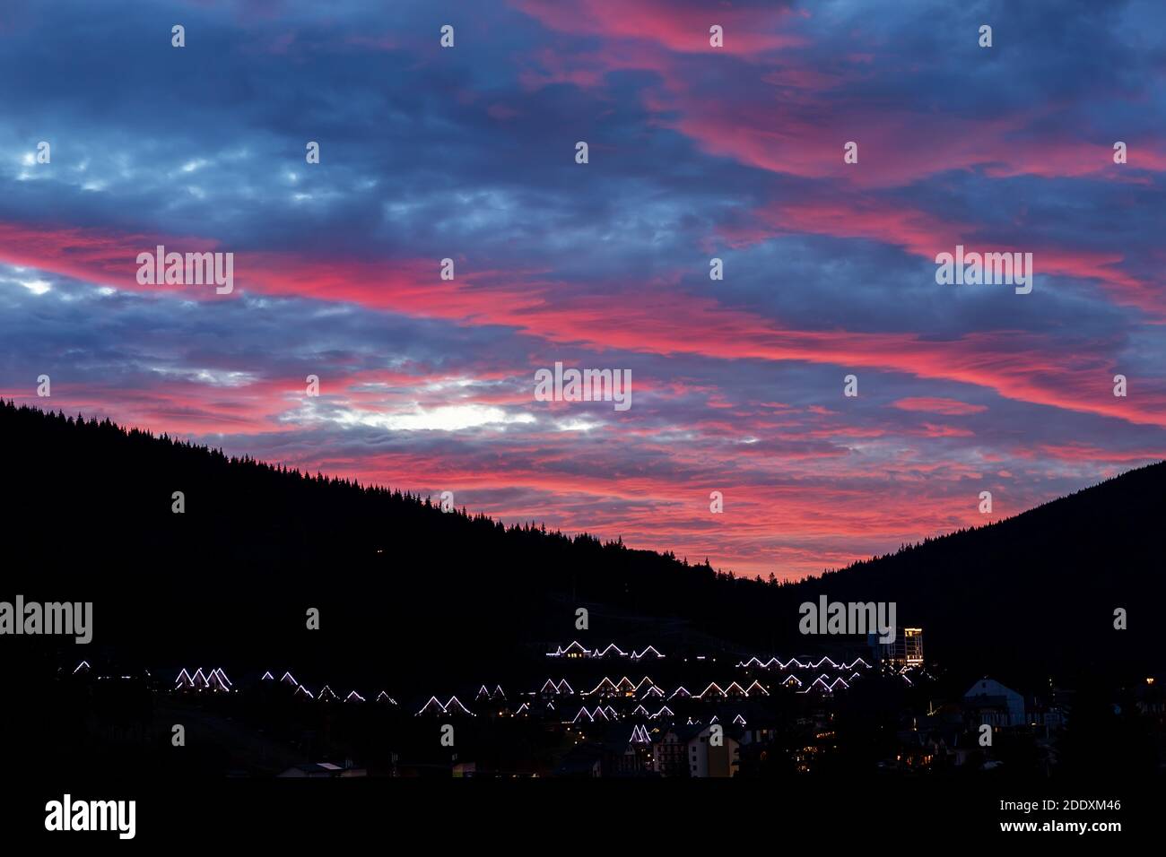 Scenografico e suggestivo tramonto nuvoloso con vista serale sulla località di montagna Villaggio Bukovel in Ucraina con le luci del tetto e l'albero della foresta sagome Foto Stock