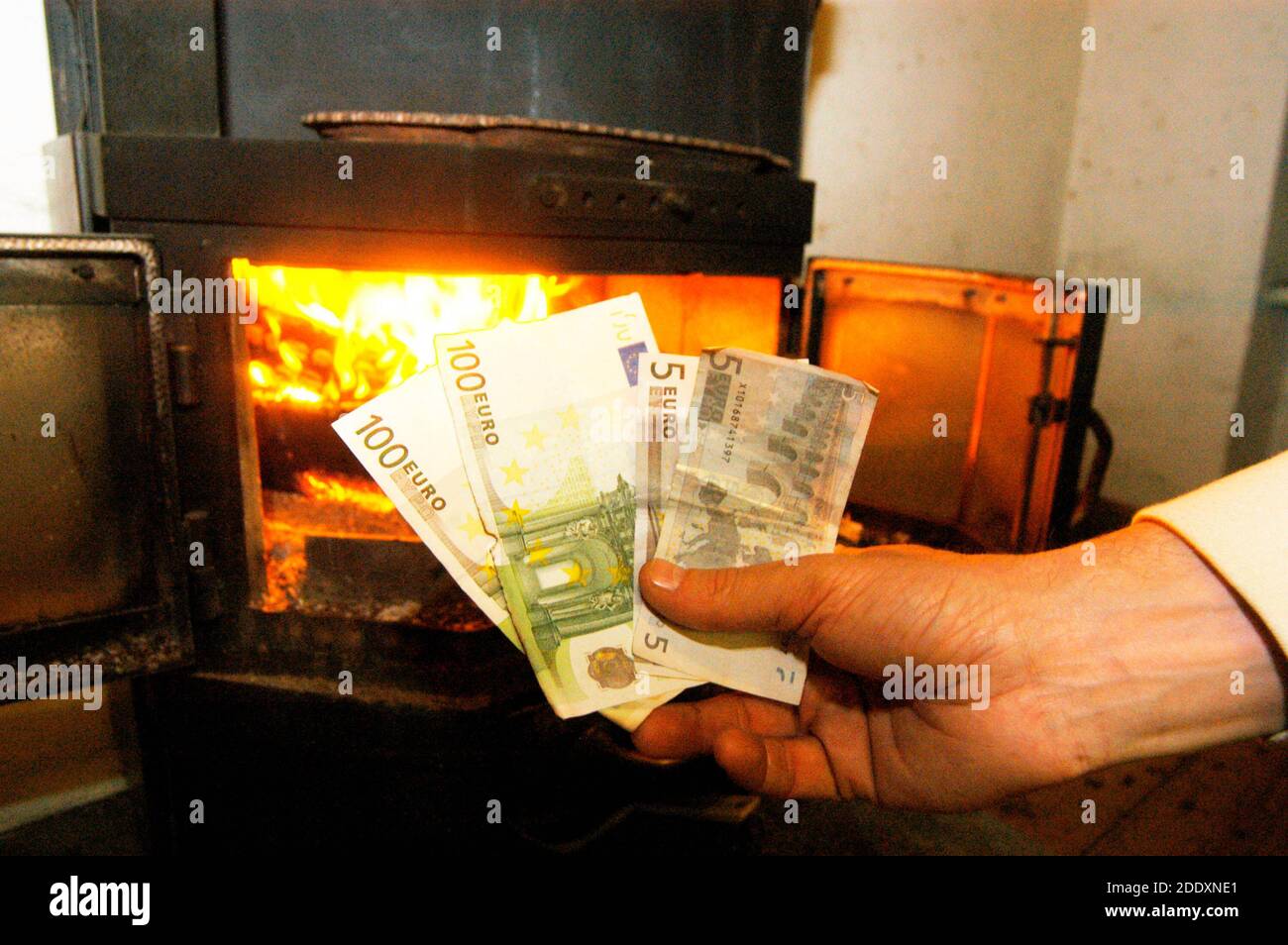 persona che tiene le banconote in contanti al fuoco del forno, simbolo per i costi di riscaldamento per la legna da ardere Foto Stock