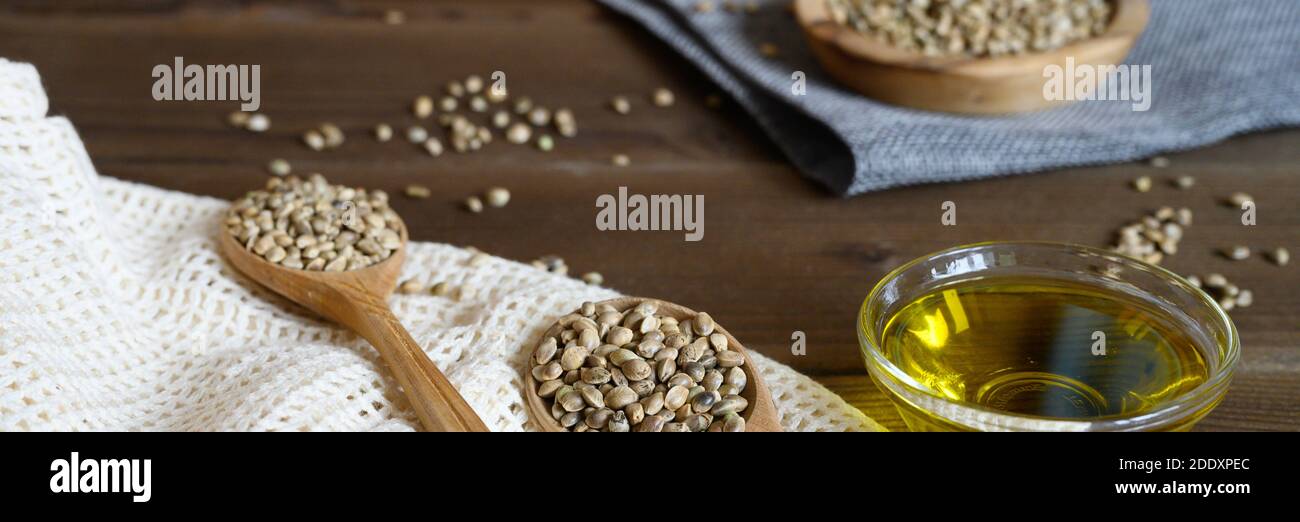 semi alimentari di canapa essiccati organici in una composizione con oggetti da cucina su uno sfondo di legno. banner Foto Stock
