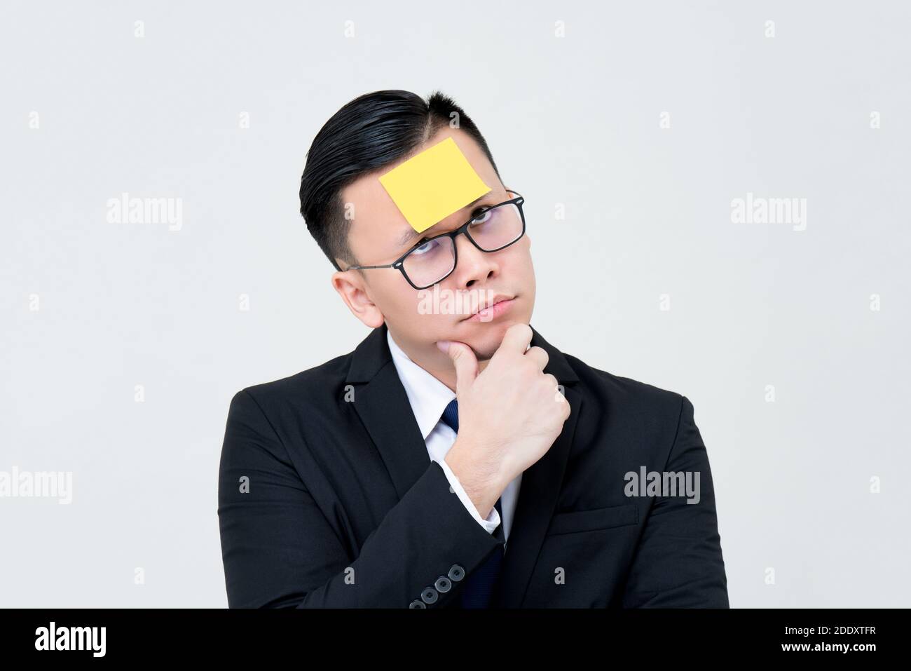 Annoiato e curioso uomo d'affari asiatico pensare con carta di nota appiccicosa sulla fronte isolato su sfondo grigio chiaro Foto Stock