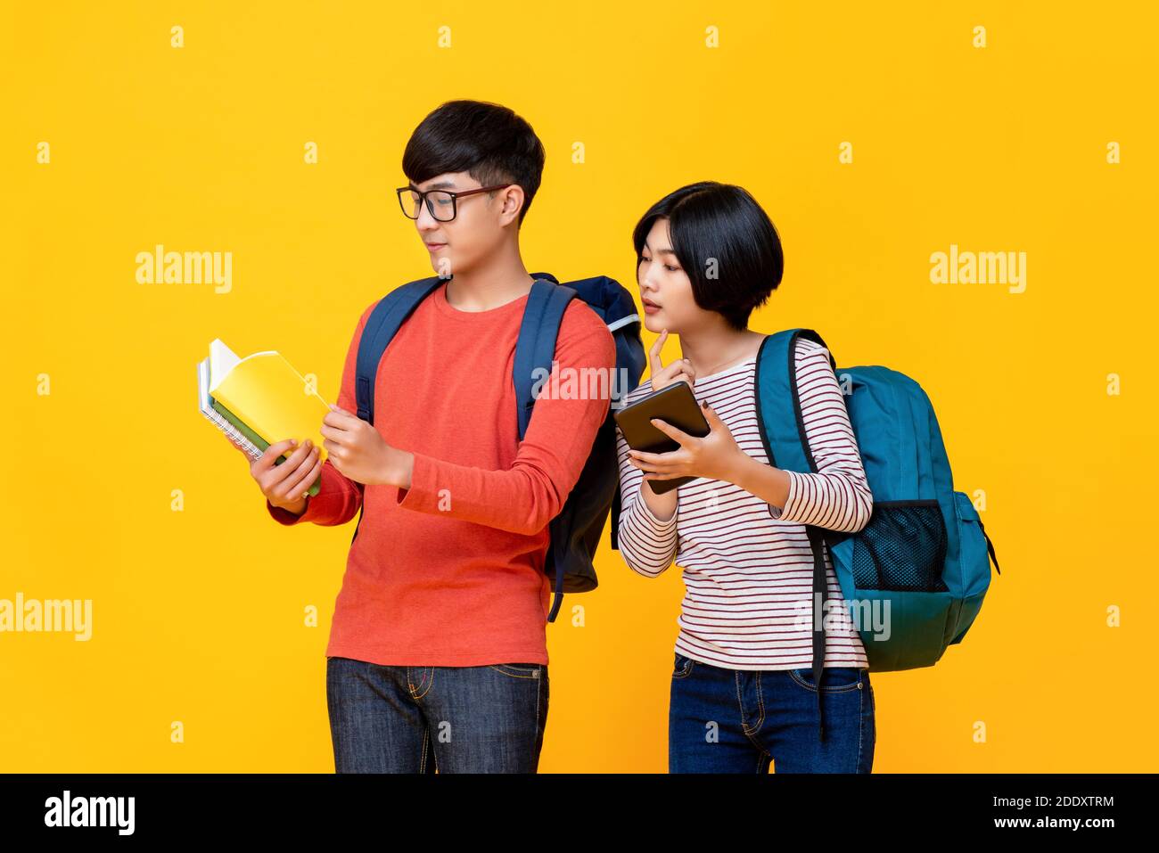 Giovani studenti asiatici maschi e femmine in colorati abiti casual guardando il libro isolato sfondo giallo per il concetto di educazione Foto Stock