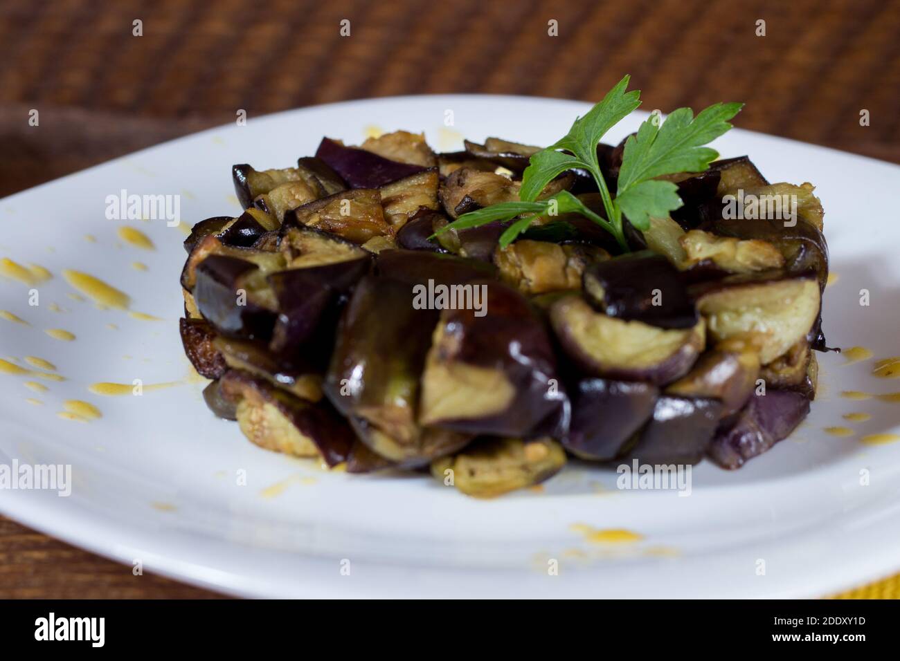 Piatto di melanzane a dadini su una crema di pomodori ciliegini gialli in un piatto bianco. Legno di fondo. Messa a fuoco selettiva. Foto Stock
