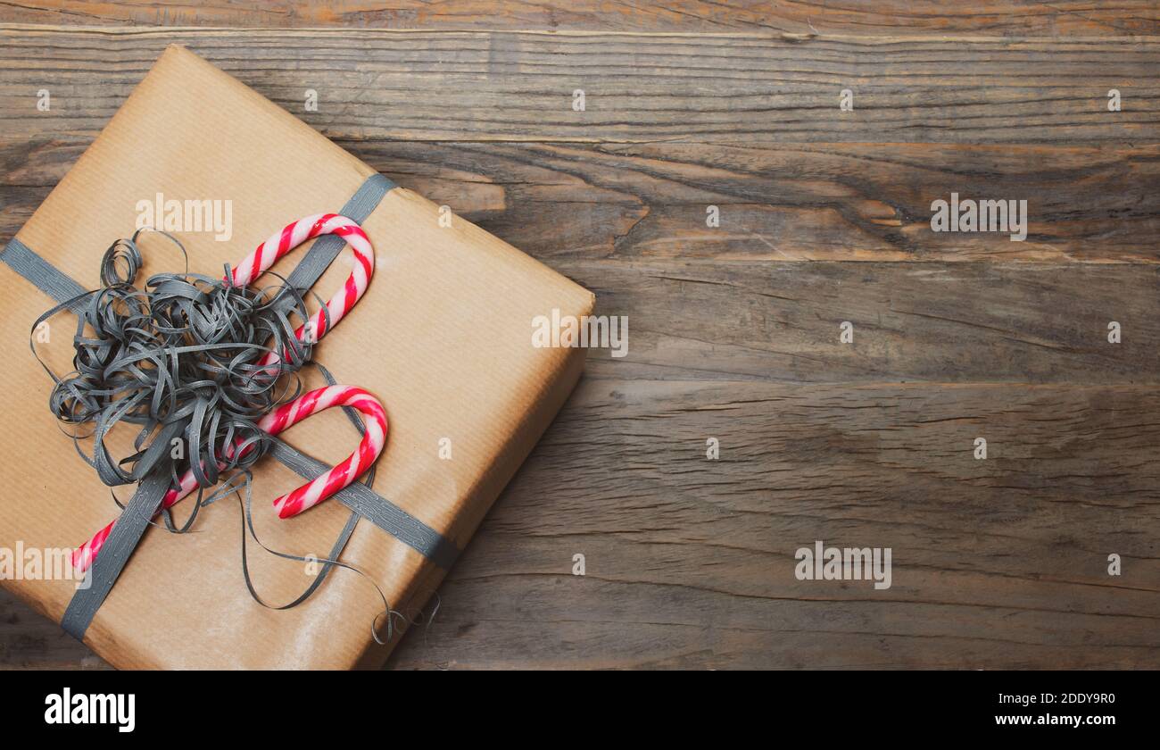 Scatola regalo marrone con nastro e canna caramella su sfondo di legno. Foto Stock