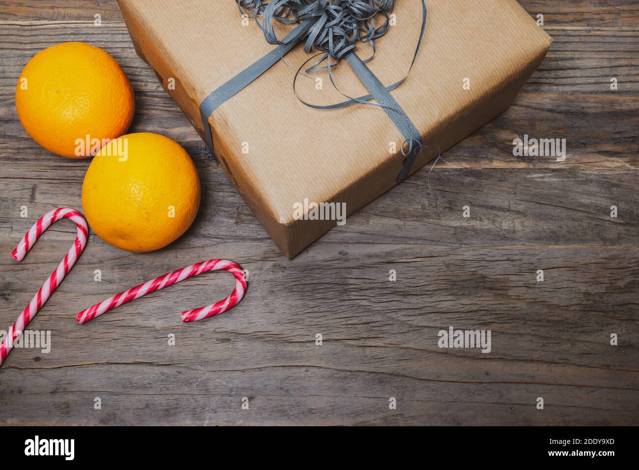 Concetto di San Nicola con scatola regalo marrone, arance e canne caramelle a strisce su sfondo di legno. Foto Stock