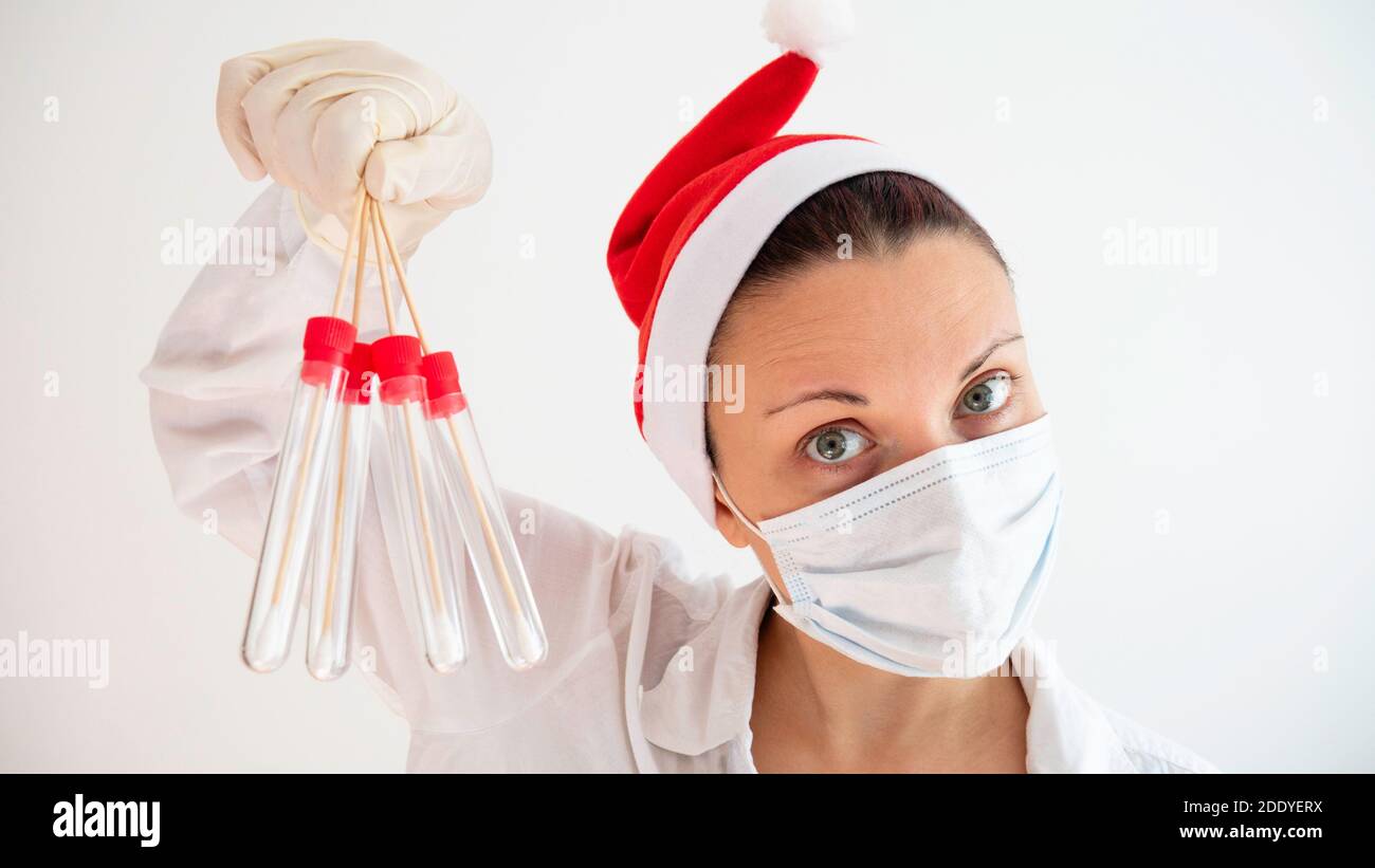 Una donna medico con un cappello Babbo Natale, maschera medica e guanti in lattice può contenere quattro provette. Stagione influenzale. Corona virus durante le vacanze. Foto Stock