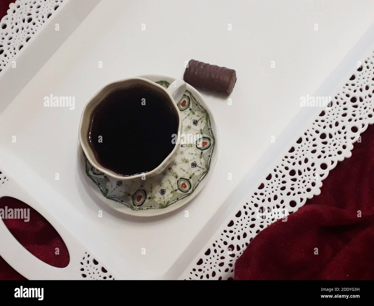 Caffè del mattino in una piccola tazza di porcellana con un grazioso pattern e showcolade caramelle su un vassoio bianco nel letto Foto Stock