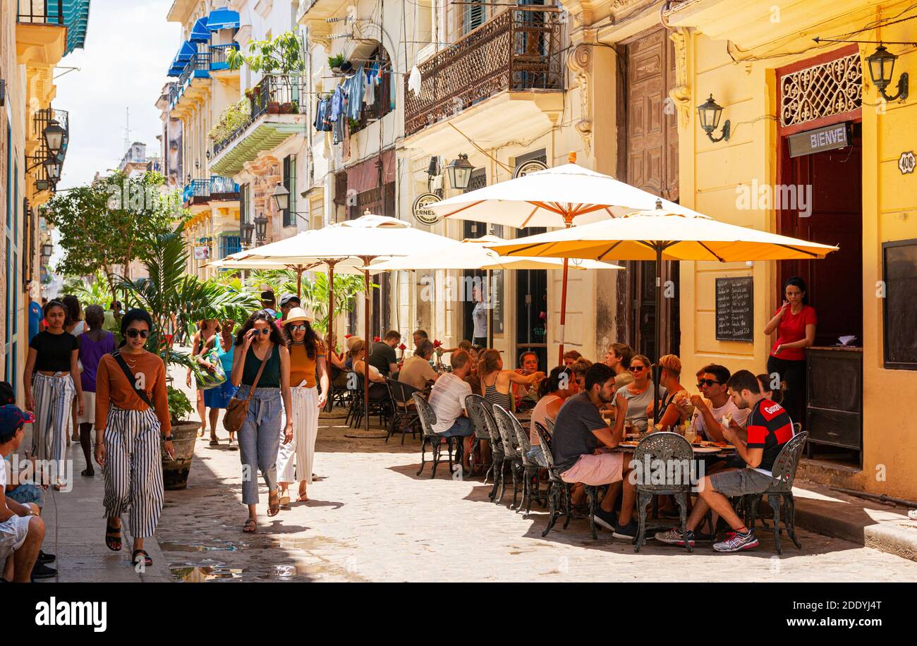 L'Avana, Cuba - 26 luglio 2018: Una strada con tavoli allestiti sotto gli ombrelloni fuori ristoranti per i turisti e la gente del posto a godersi la giornata. Foto Stock