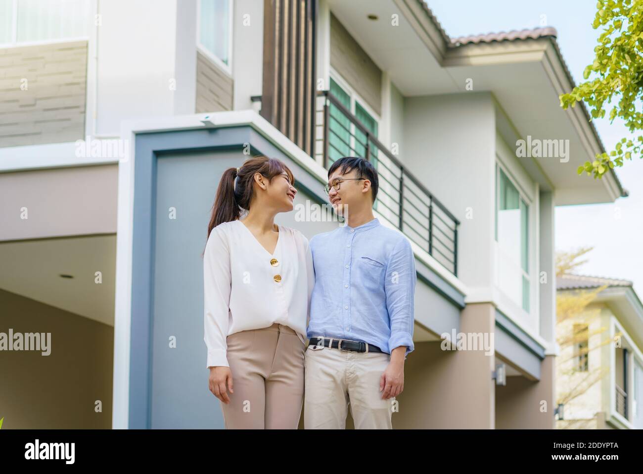 Ritratto di giovane coppia asiatica in piedi e abbracciando insieme guardando felice di fronte alla loro nuova casa per iniziare la nuova vita. Famiglia, età, casa, vera esta Foto Stock