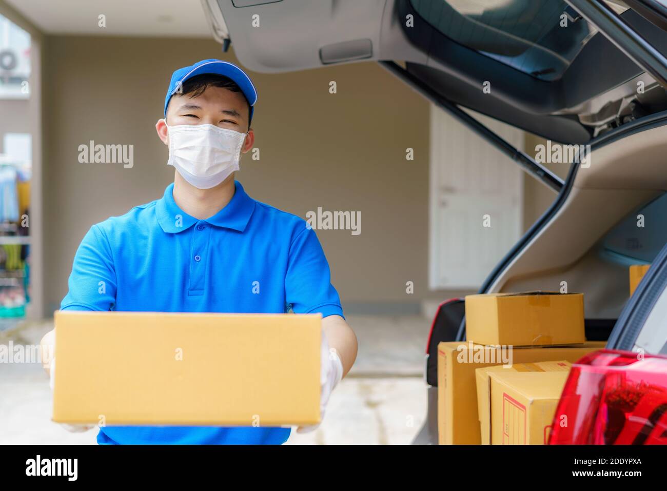 Asian Delivery uomo servizi corriere lavorando con scatole di cartone su furgone durante la pandemia di Coronavirus (COVID-19), corriere che indossa maschera medica e l Foto Stock