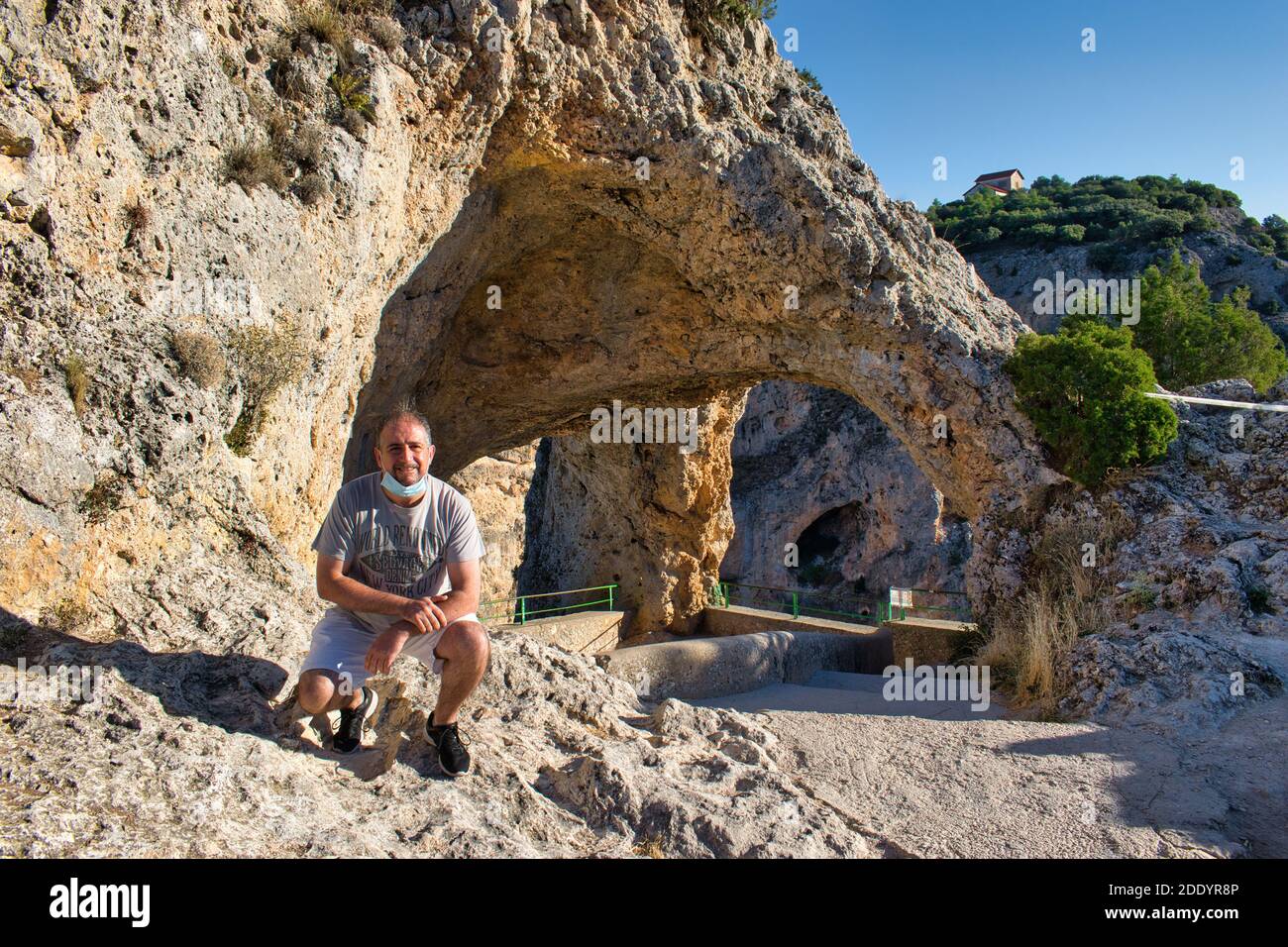 Uomo adulto con maschera in vista del Ventano del Diablo a Cuenca con arco e ponte naturale di roccia, Spagna Foto Stock