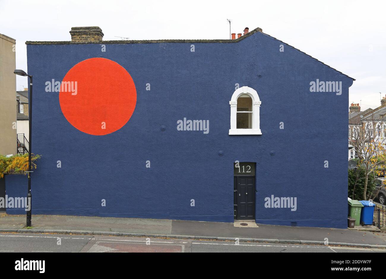 Parete laterale di una casa londinese dipinta di blu scuro con un grande cerchio rosso. Lyndhurst Grove, Peckham, Londra, Regno Unito. Foto Stock
