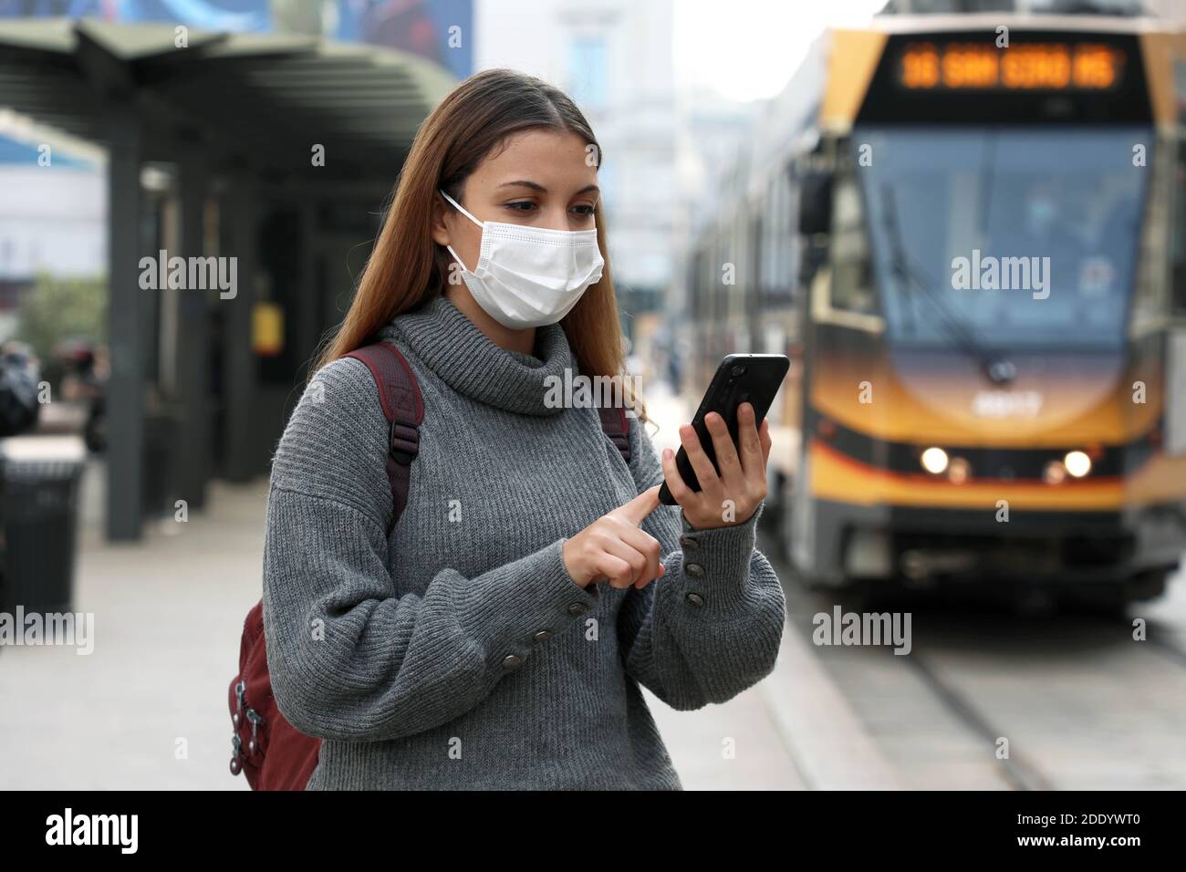 Giovane donna con maschera protettiva che acquista e paga per in linea biglietto di trasporto tramite l'applicazione bancaria sullo smartphone in via cittadina Foto Stock