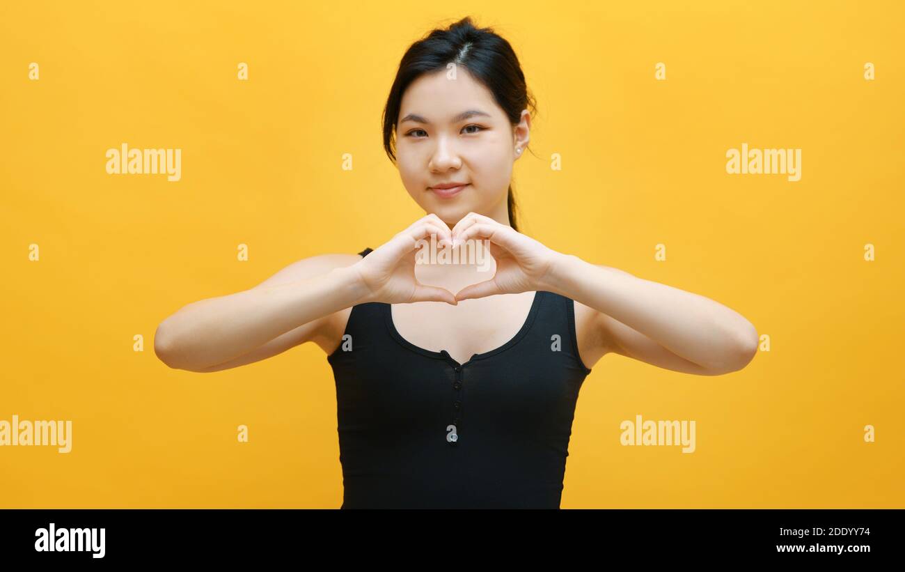 Bella giovane donna asiatica che fa il cuore forma con le mani. Isolato su sfondo giallo. Foto di alta qualità Foto Stock