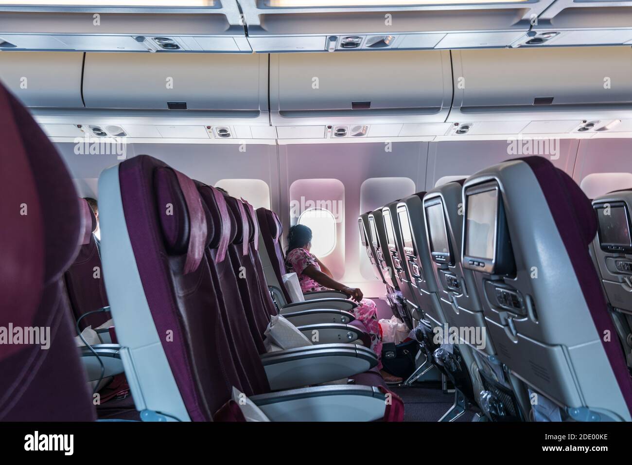 Una donna indiana che guarda la finestra di aeroplano di Qatar Airways nel cielo blu che vola a Doha Foto Stock