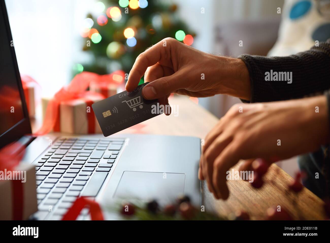 Concetto di persona che fa shopping di natale in linea a casa da un laptop con scheda. Vista frontale. Composizione orizzontale. Foto Stock